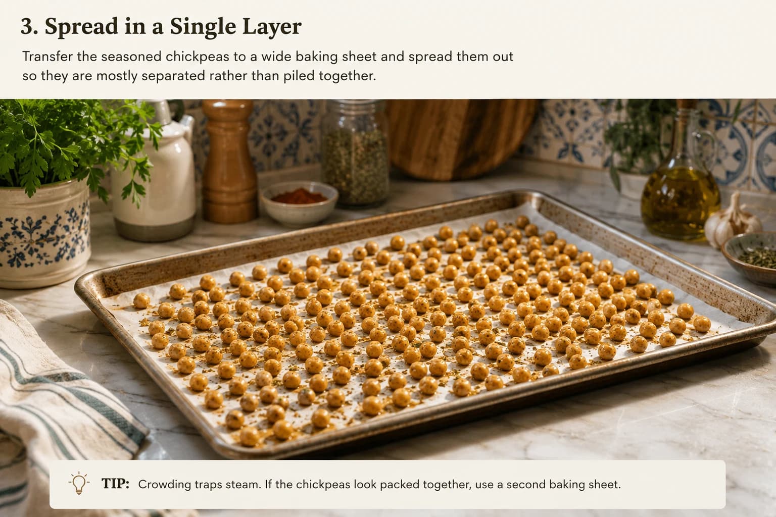 Seasoned chickpeas spread in a loose single layer on a baking sheet in a stylish Mediterranean kitchen.