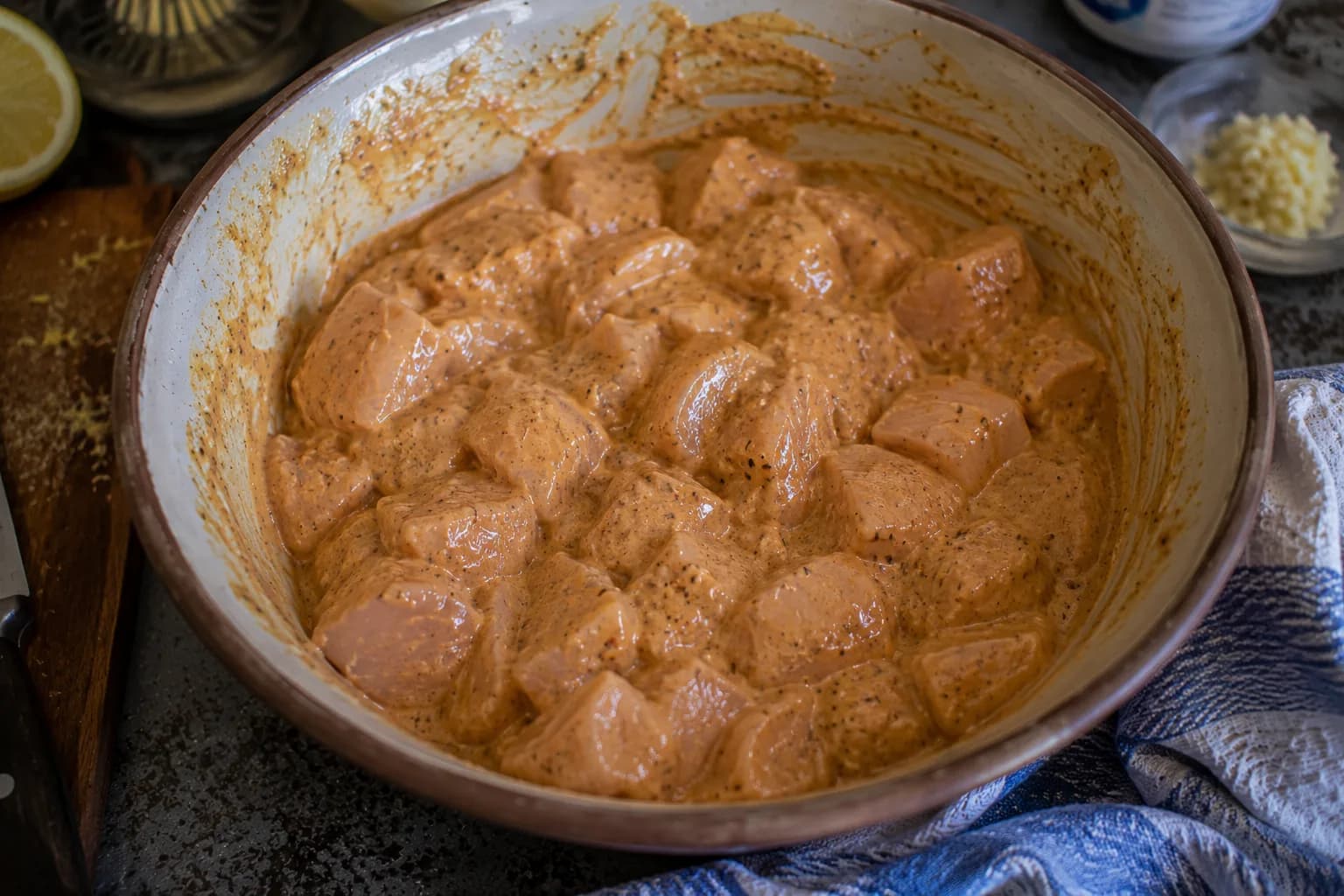 Chicken cubes completely coated in a reddish yogurt marinade and resting before grilling.
