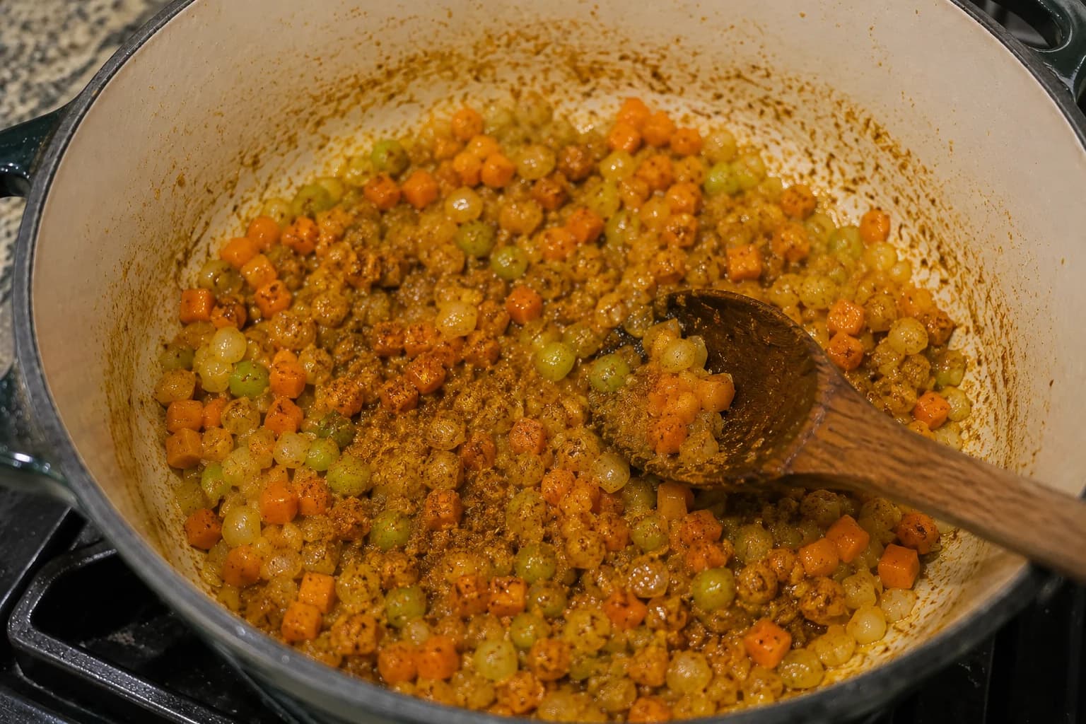 Cumin, coriander, and turmeric being stirred into sautéed vegetables.